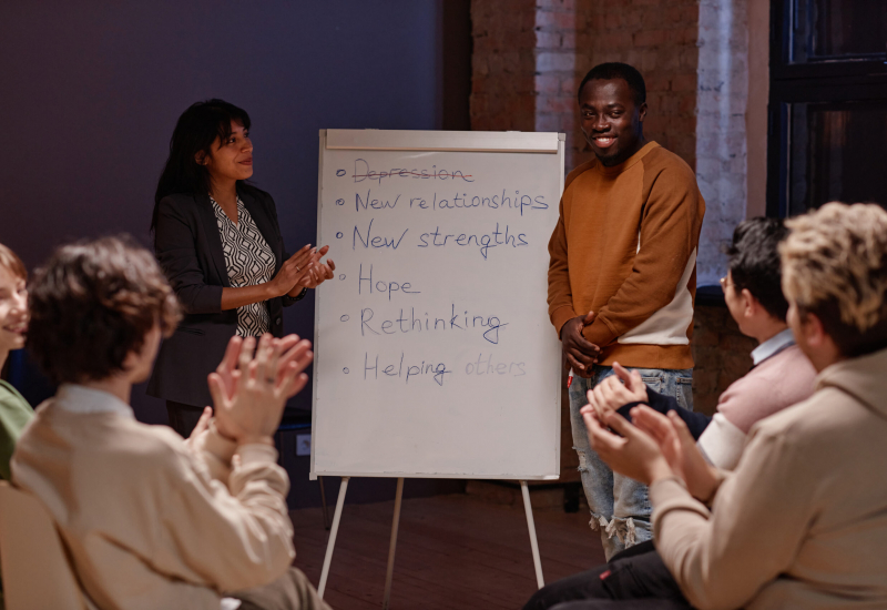 Horizontal shot of people clapping hands to joyful Black man successfully finishing depression treatment with help of group therapy